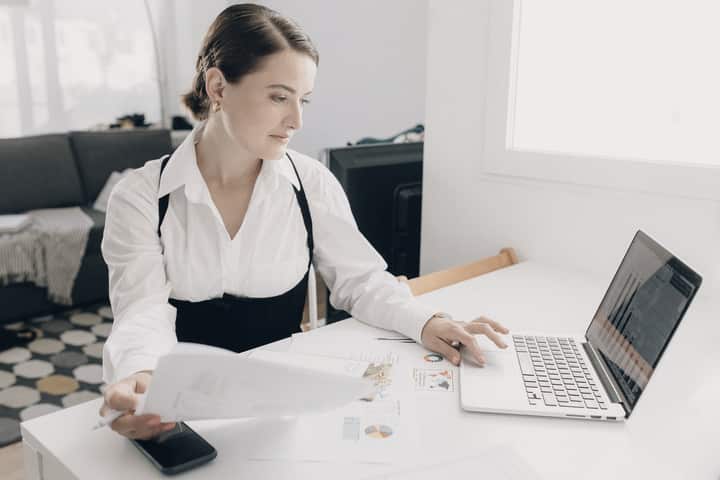 A woman reviewing a printed report beside her laptop.