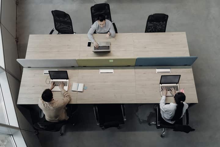 Colleagues working at shared office tables with laptops and notes.